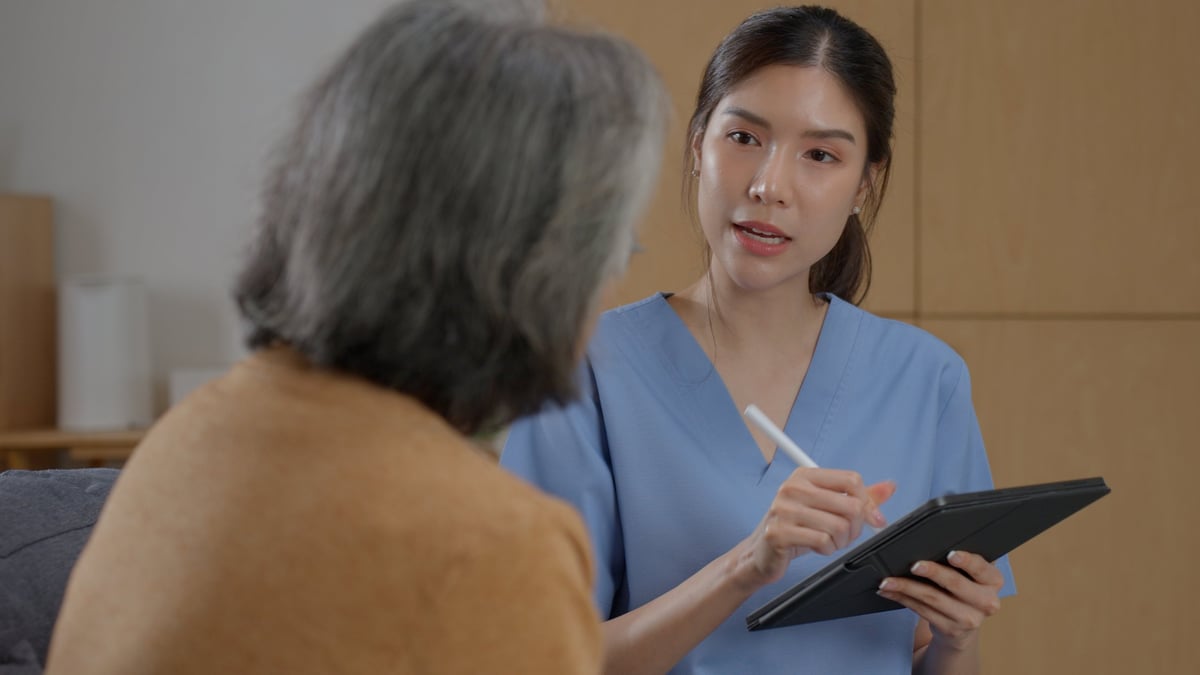 A nurse documenting patient information on a tablet while speaking with a patient